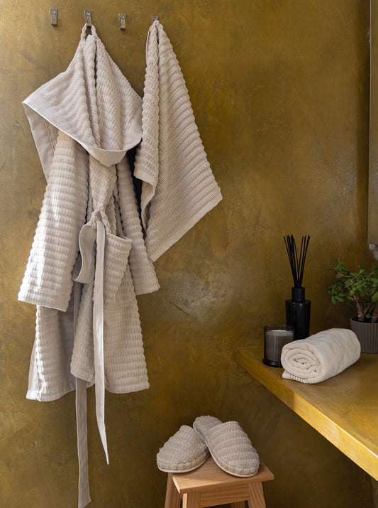 Beige Swell organic cotton bathrobe displayed on a hanger, showcasing its soft texture and elegant design with a tie belt and spacious pockets.